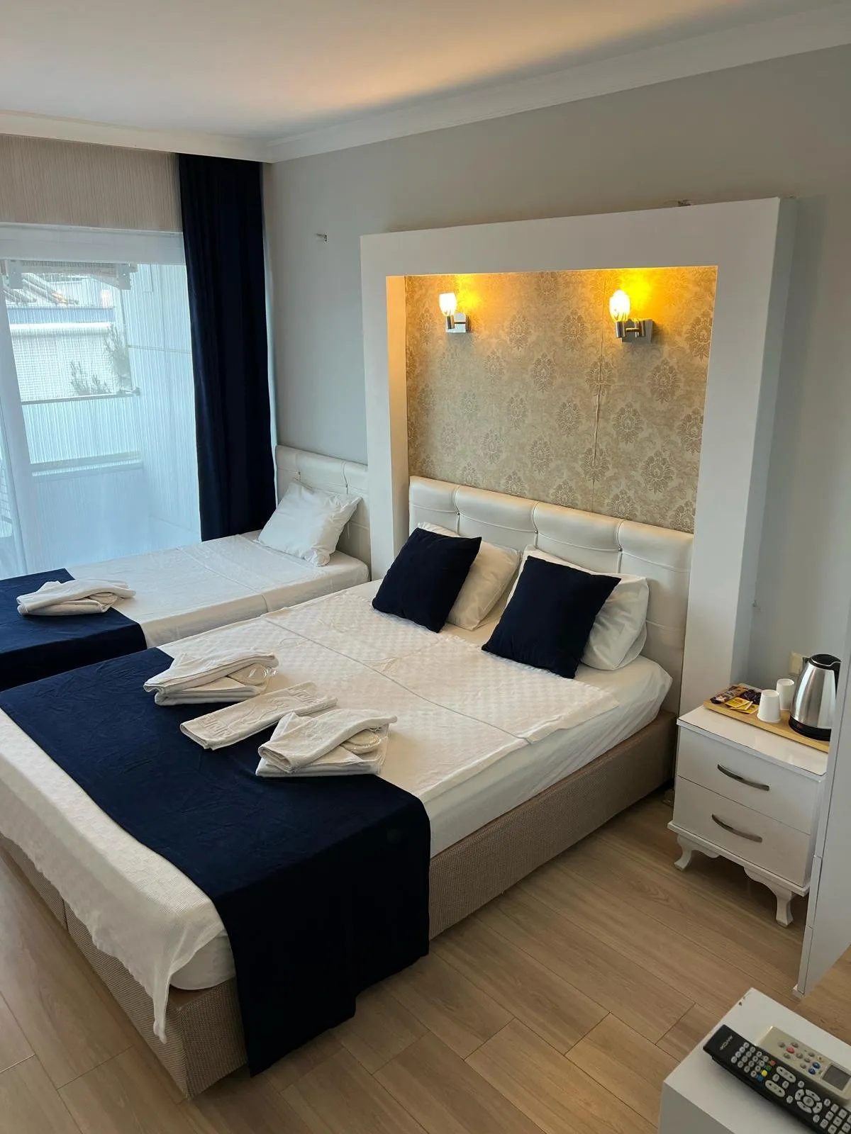 Standart odanın genel görünümü — yatak, TV ünitesi ve balkon kapısı
